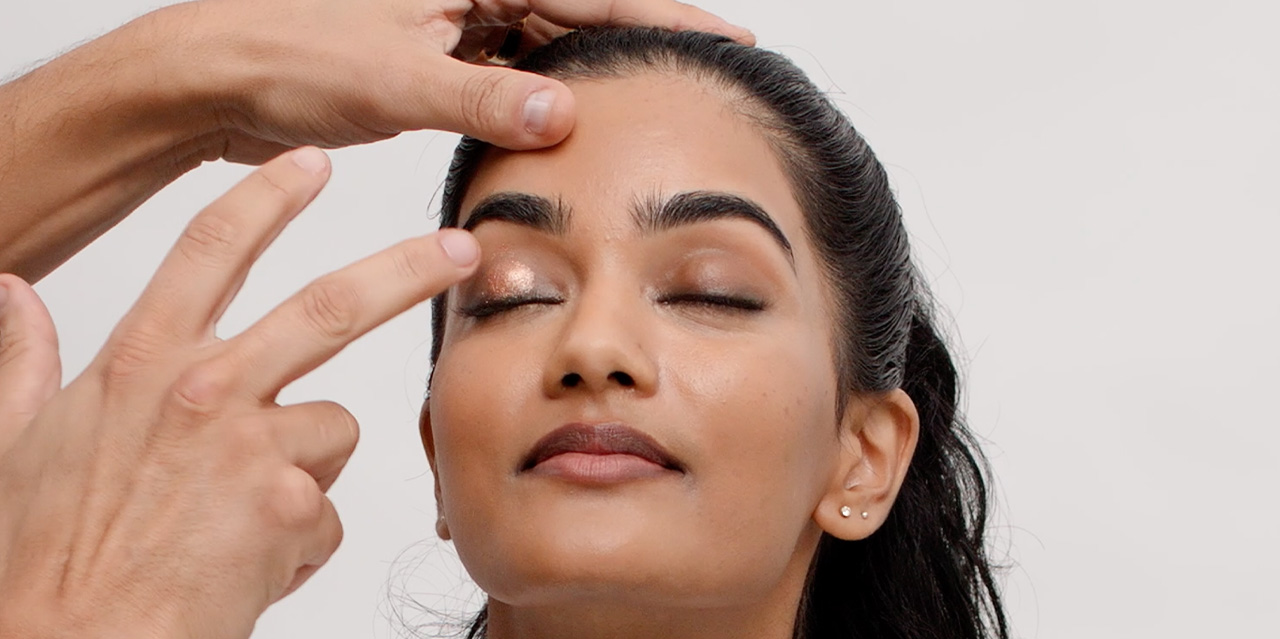 Makeup artist applying shimmery eyeshadow for model’s brown smokey eye